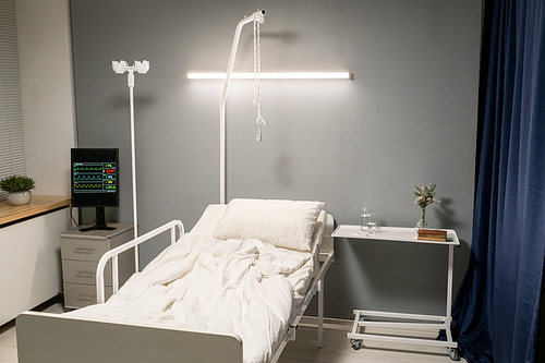 Image of empty bed for patient with dropper and lamp that disinfecting the hospital ward