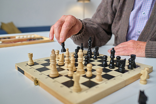 Close-up of senior man sitting at the table and playing chess during his leisure time