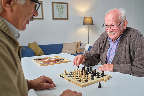 Two elderly men playing chess together at the table during leisure time in nursing home