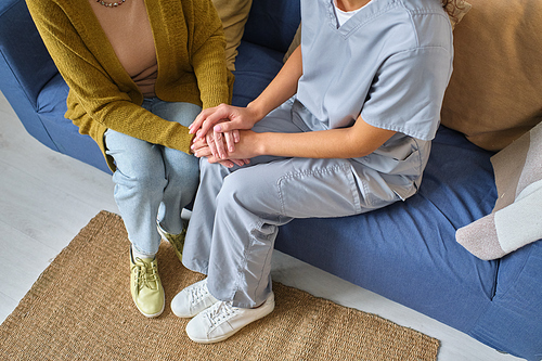 Close-up of nurse holding hands of senior woman while they sitting on sofa, she looking after senior people