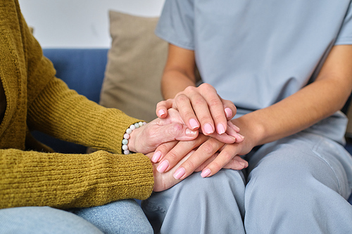 Close-up of nurse in uniform holding hands of elderly woman, she supporting her during her disease