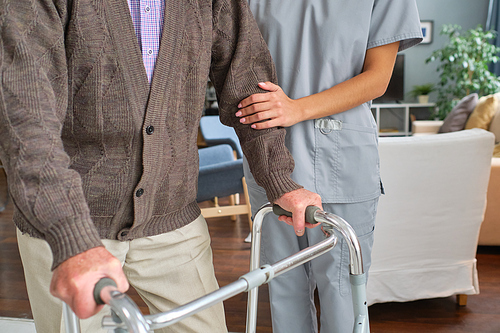 Close-up of elderly man moving with the help of a walker with nurse walking with him