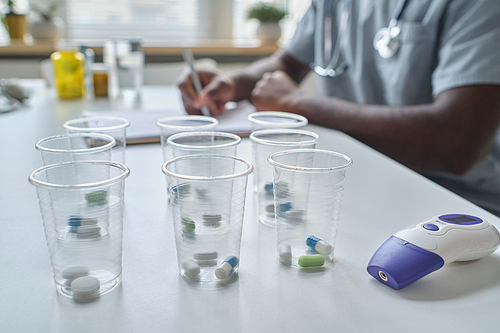 Close-up of glasses with pills inside of them standing on the table at hospital with doctor in the background