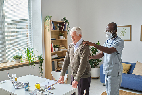 African doctor in uniform examining the elderly man during his visit at doctors office