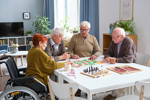 Group of senior people sitting at the table and playing board games together in nursing home