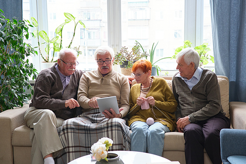 Elderly people sitting on sofa and using digital tablet together during their leisure time in the room