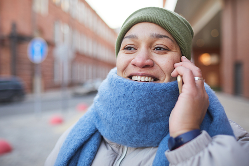 Close-up of woman in warm scarf smiling while talking on mobile phone outdoors