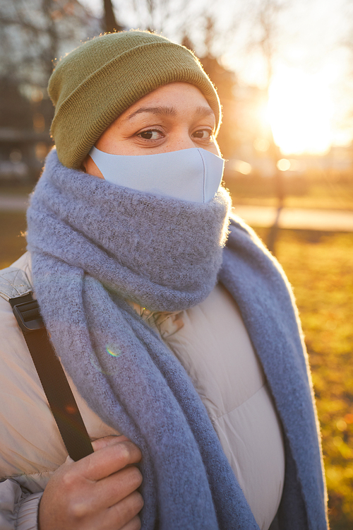 Portrait of young woman in protective mask walking outdoors in cold weather