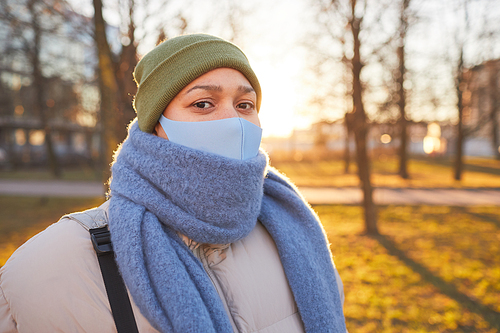 Portrait of young woman in protective mask looking at camera while walking in the city