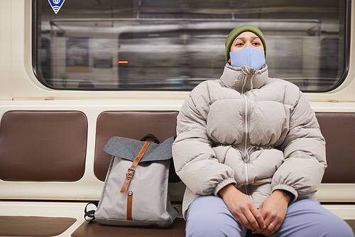 Young woman in mask and in warm clothing sitting on a train underground