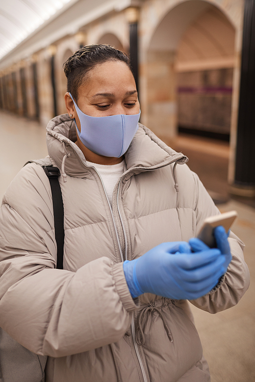 Young woman in protective mask and gloves talking online on mobile phone while walking in underground