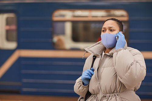 Woman in protective mask and gloves has a conversation on mobile phone while standing in underground