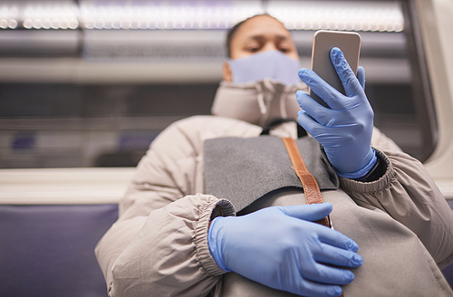 Young woman in protective mask and gloves sitting on a train and using her mobile phone during the trip