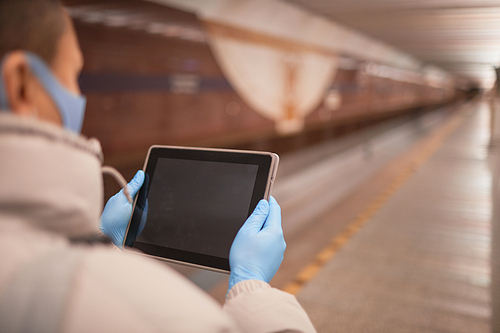 Rear view of woman in protective mask and in protective gloves holding digital tablet and reading online