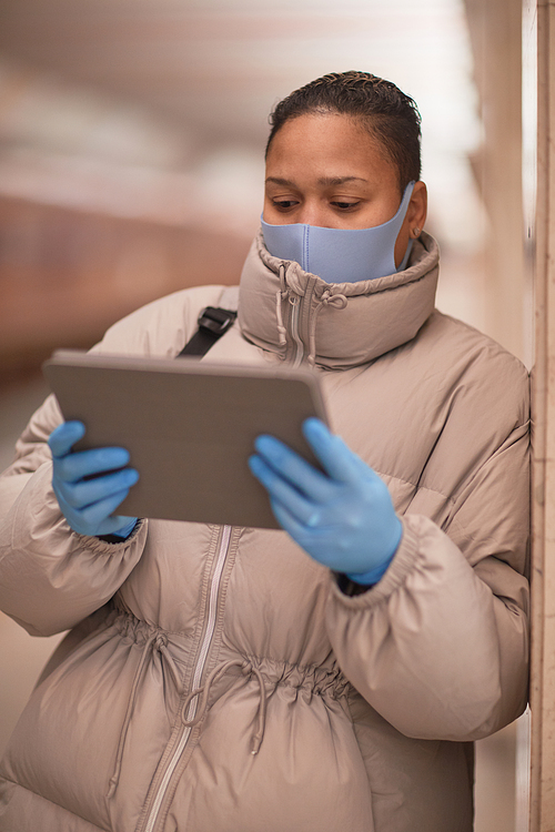 Young woman in mask and in protective gloves using digital tablet while waiting for the train