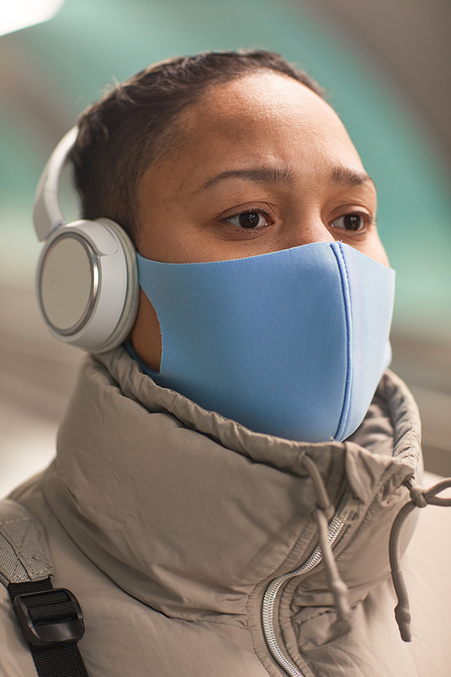 Close-up of woman in wireless headphones and in protective mask listening to music