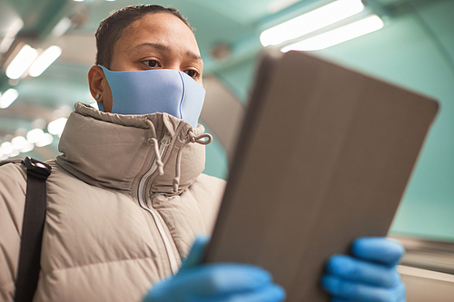 Close-up of woman in warm clothing and in protective mask and gloves working online on digital tablet