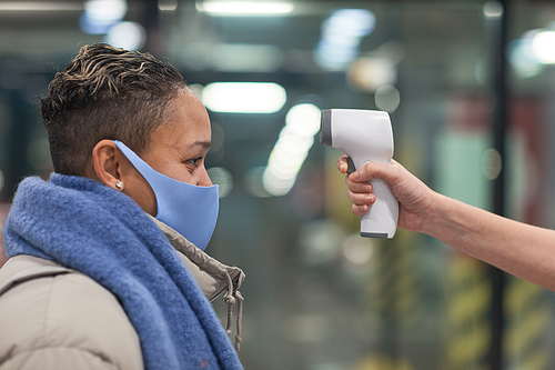 Side view of woman in protective mask checking her temperature before entering in supermarket