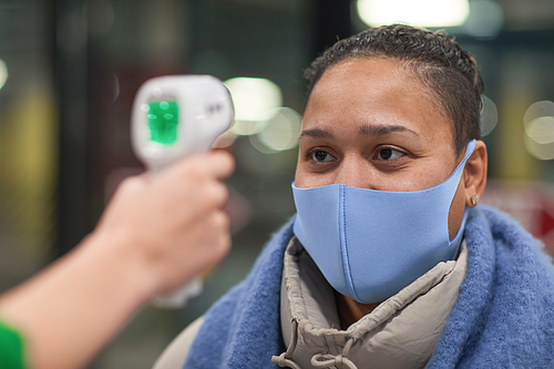 Young woman in protective mask checking the temperature before entering during pandemic