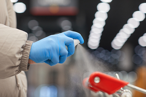 Close-up of woman in protective gloves applying antiseptic on the handle of shopping cart in the shop