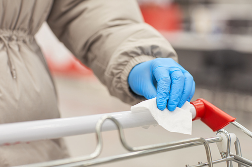 Close-up of woman in protective gloves wiping the dirt with napkin on the shopping cart