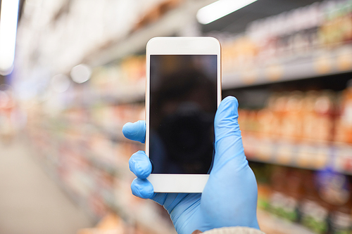 Close-up of woman in protective gloves holding mobile phone and making a photo in supermarket