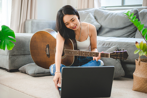 Asian woman playing music by guitar at home, young female guitarist musician lifestyle with acoustic art instrument sitting to play and sing a song making sound in hobby in the house room
