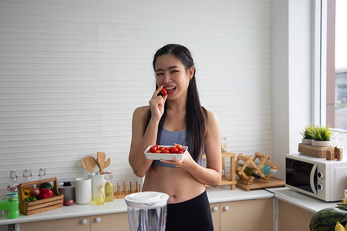 young Asian woman cooking vegetable healthy food and eating or drinking in home kitchen