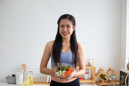 young Asian woman cooking vegetable healthy food and eating or drinking in home kitchen