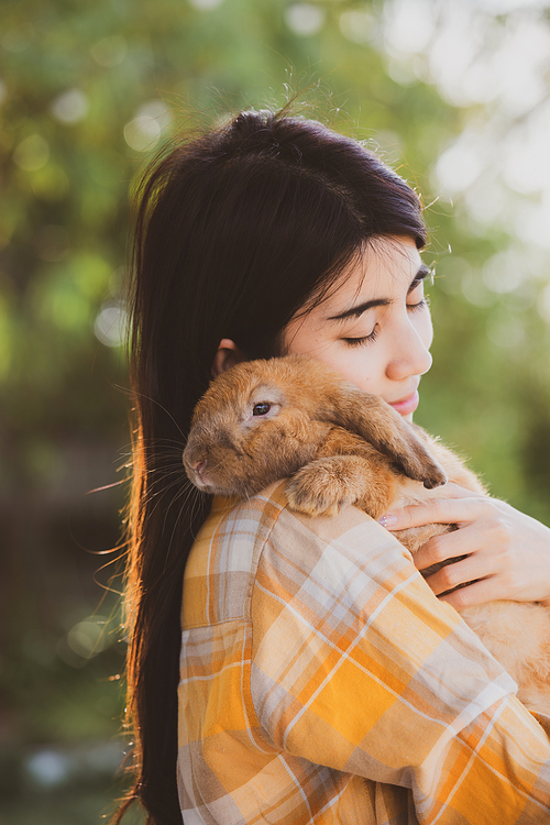 Young smiling and innocent girl holding and hugging a cute little rabbit with closed eyes and caressing her on back