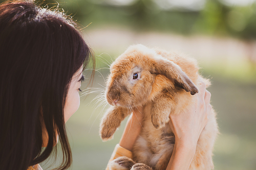 Young smiling and innocent girl holding and hugging a cute little rabbit with closed eyes and caressing her on back