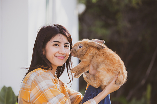 Young smiling and innocent girl holding and hugging a cute little rabbit with closed eyes and caressing her on back