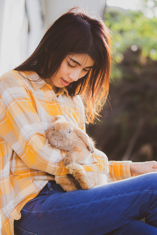 Young smiling and innocent girl holding and hugging a cute little rabbit with closed eyes and caressing her on back