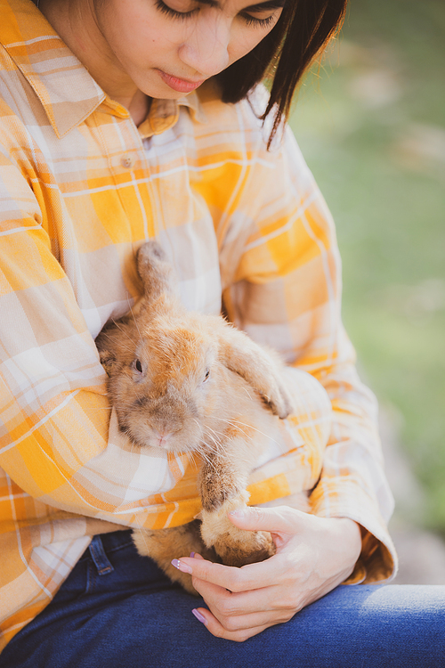 Young smiling and innocent girl holding and hugging a cute little rabbit with closed eyes and caressing her on back