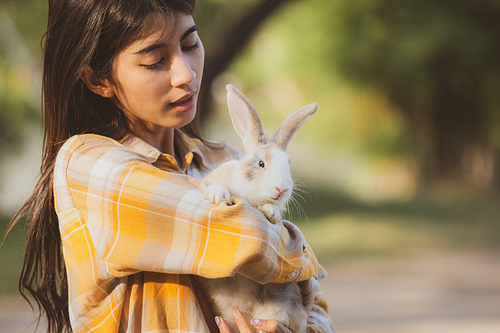 beautiful pretty portrait of young Asian woman person with cute rabbit in pet and animal care concept, happy female holding bunny at nature outdoor field with friendship, easter concept