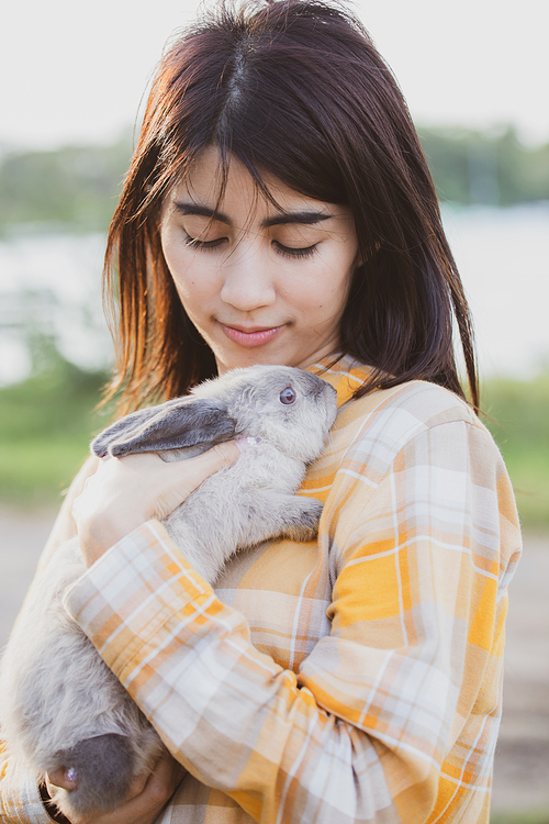 beautiful pretty portrait of young Asian woman person with cute rabbit in pet and animal care concept, happy female holding bunny at nature outdoor field with friendship, easter concept