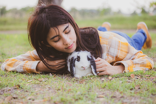 beautiful pretty portrait of young Asian woman person with cute rabbit in pet and animal care concept, happy female holding bunny at nature outdoor field with friendship, easter concept