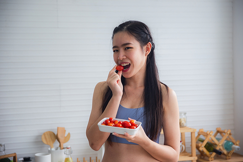Fit and healthy young Asian woman in sportswear preparing and drinking fresh lemon water for healthy lifestyle and fitness in modern kitchen after morning workout and exercise at home
