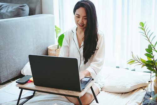 young Asian woman using laptop computer to business online work, female freelance working from home by using internet cyberspace communication technology for businesswoman job