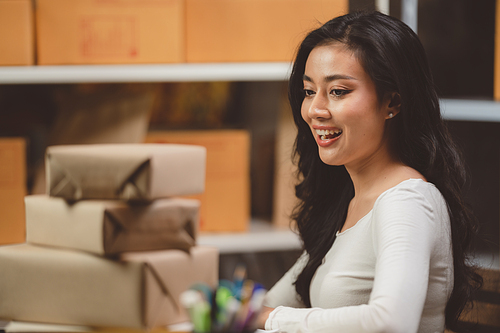 Smiling and successful young female Asian warehouse manager and worker working in storage house while checking package and parcel and placing in shelf and rack