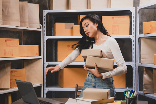 Smiling and successful young female Asian warehouse manager and worker working in storage house while checking package and parcel and placing in shelf and rack