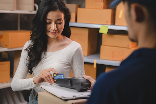 credit card and wireless POS terminal for card payment concept, Young Asian girl with a credit card received a parcel from a male delivery man The woman paid the male delivery man