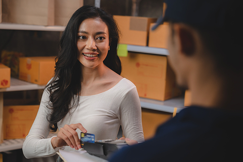 credit card and wireless POS terminal for card payment concept, Young Asian girl with a credit card received a parcel from a male delivery man The woman paid the male delivery man