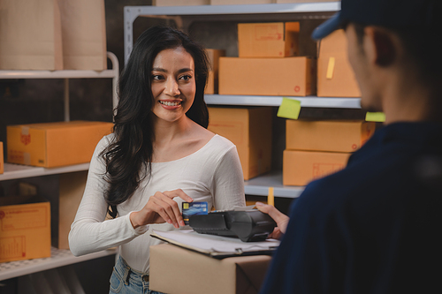 credit card and wireless POS terminal for card payment concept, Young Asian girl with a credit card received a parcel from a male delivery man The woman paid the male delivery man