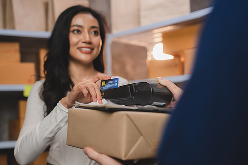 credit card and wireless POS terminal for card payment concept, Young Asian girl with a credit card received a parcel from a male delivery man The woman paid the male delivery man