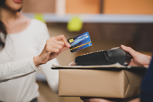 credit card and wireless POS terminal for card payment concept, Young Asian girl with a credit card received a parcel from a male delivery man The woman paid the male delivery man