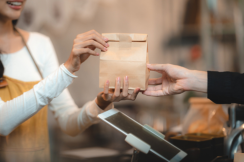 Bakery and coffee cafe business shop concept, Asian female wearing aprons, happily smiling to serving breakfast baked bread, beautiful woman staff service customer to delivery a food