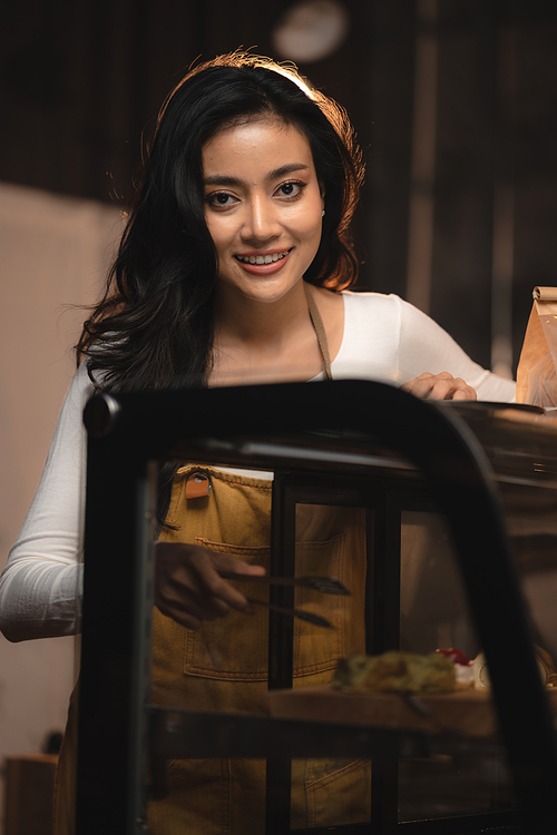 Bakery and coffee cafe business shop concept, Asian female wearing aprons, happily smiling to serving breakfast baked bread, beautiful woman staff service customer to delivery a food