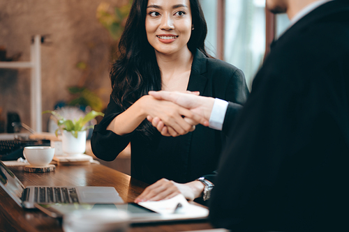 Smiling and laughing young Asian successful business woman discussing work with male colleague and partner in modern office while using digital tablet