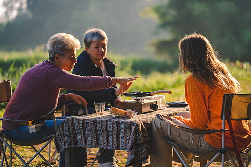 woman family having fun with food of picnic camp in the nature morning, summer travel vacation lifestyle of mother and girl at adventure forest park landscape in holiday, outdoors activity breakfast